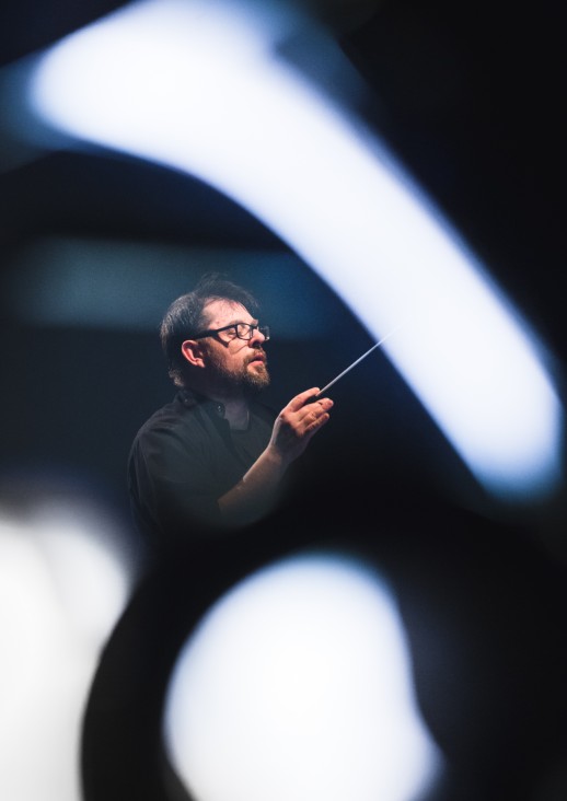 portret mężczyzny w okularah trzymającego w dłoni batutę