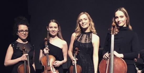 four young women in dark dresses standing and holding string instruments