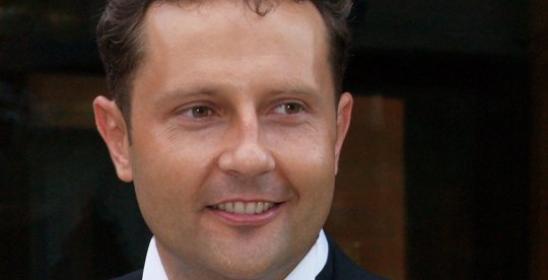 A man in a white shirt and black jacket, with a rose in his buttonhole