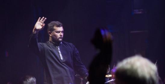 młody mężczyzna z uniesioną ręka dyrykujący orkiestrą