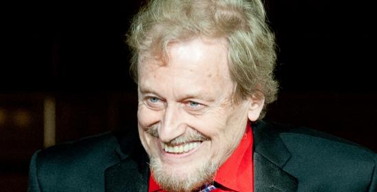 An older man in a red shirt and tuxedo