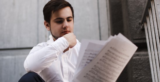 ciemnowłosy mężczyzna w białej koszuli trzymający nuty