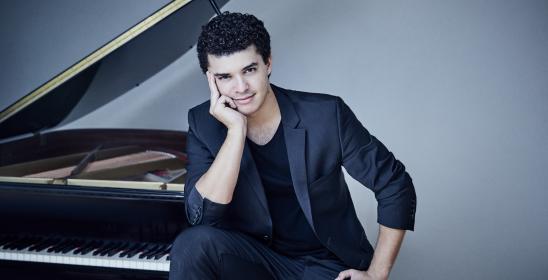 young dark-haired man sitting next to the piano