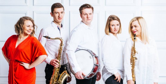 five people - a woman in a red dress, a man and a woman holding saxophones, a man holding a snare drum