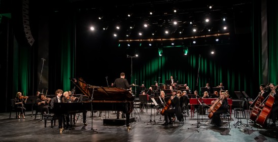 pianista siedzi przy fortepianie i orkiestra siedząca na scenie
