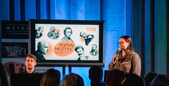 kobieta mowiąca do mikrofonu, obok na wyświetlaczu pokazana grafika dotycząca koncertów z cyklu Poznaj muzykę