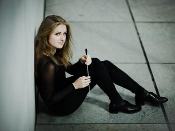 a young blonde woman sitting, leaning against the wall, holding a baton in her hand