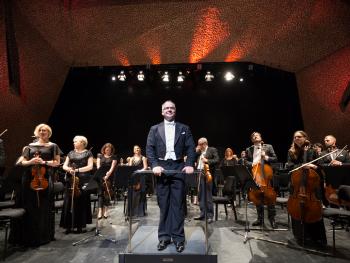 a man in a tailcoat standing on the stage in front of the orchestra