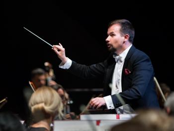 mężczyzna we fraku z batutą w prawej dłoni 