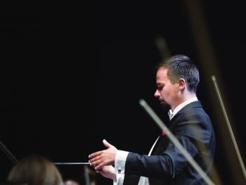 a man in a tailcoat with a baton and hands raised