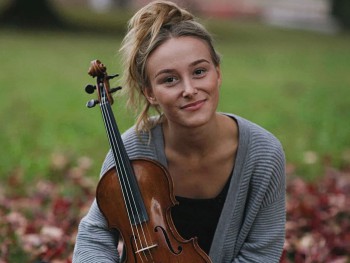 Kobieta trzymająca skrzypce siedzi na trawie