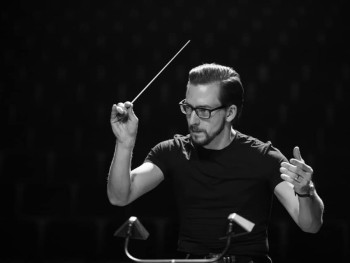 portret mężczyzny z uniesionymi rękoma trzymającego batutę