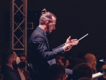 portret mężczyzny z uniesionymi rękoma trzymającego batutę