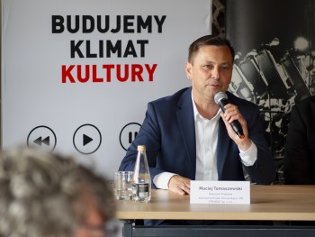 mężczyzna przemawiający do mikrofonu, w tle zapis Budujemy klimat kultury