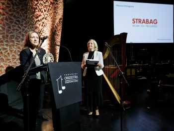 kobieta przemawiająca do mikrofonu na scenie, w tle logotyp firmy Strabag