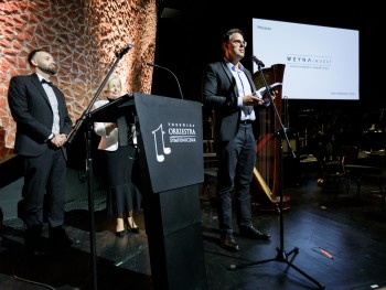 Mężczyzna przemawiający do mikrofonu na scenie, w tle logotyp Weyna Invest 