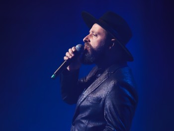 mężczyzna w kapeluszu śpiea do mikrofonu