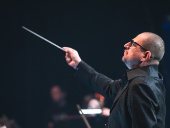 mężczyzna z uniesioną ręką, w której trzyma batutę