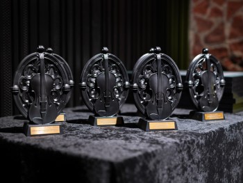 Statuetki Muza Tos-u cztery statuetki w kształcie skrzypiec wkomponowanych w okrągłe gotyckie rozety. W tle oprawione w złote ramy zdjęcie orkiestry.