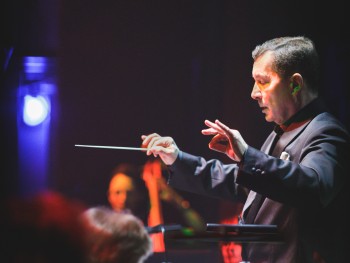 mężczyzna z uniesionymi rękoma, w jednej dłoni trzya batutę